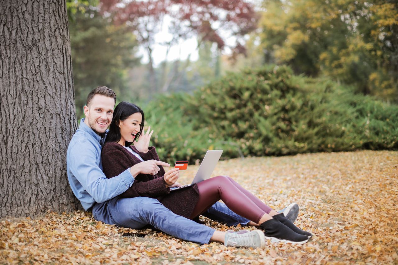 services-03 A joyful couple using a laptop and credit card outdoors during fall.