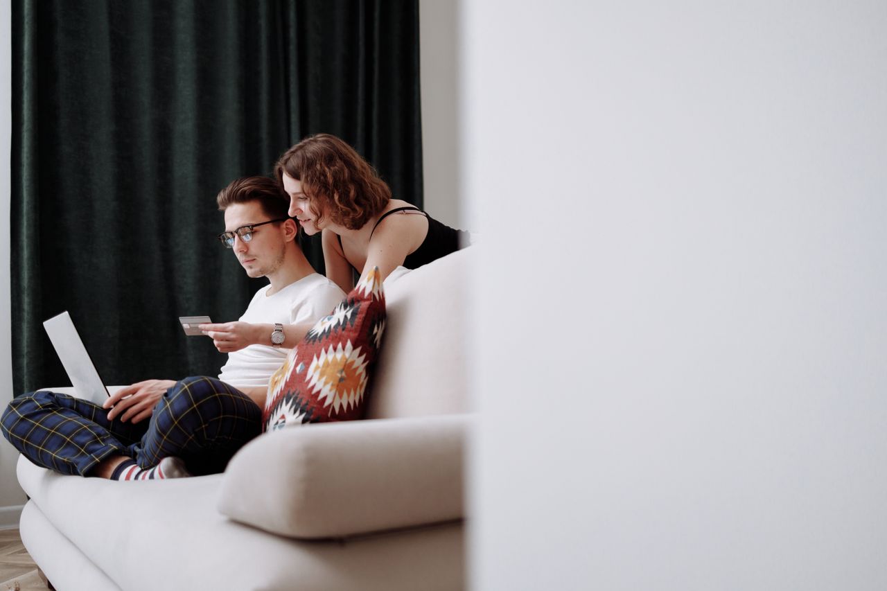 hero-img-02 A couple sits comfortably on the couch while shopping online together.
